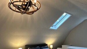A bedroom with a sloped ceiling, a skylight, a bed with striped bedding, bedside lamps, and a white dresser.
