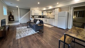 A modern kitchen with white cabinets, a grey sofa, and a dining table.