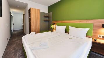 Una habitación de hotel con una cama grande, un armario de madera, una pared de acento verde y una mesita de noche con una lámpara.