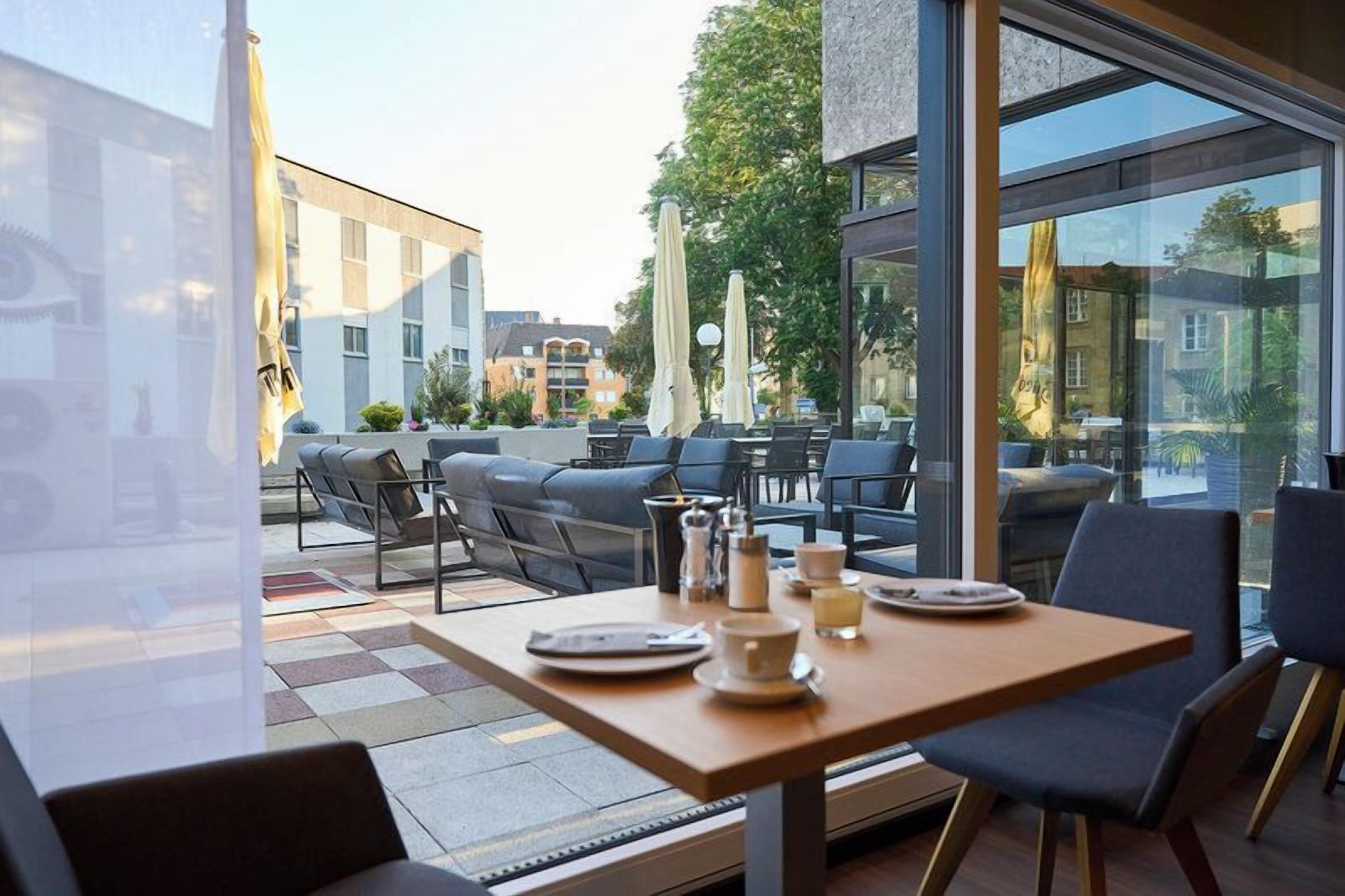 An outdoor seating area with tables and chairs, a view of the city, and a modern building facade.