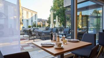 An outdoor seating area with tables and chairs, a view of the city, and a modern building facade.