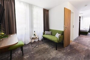 A room with a green sofa, a small round table with a bottle, a wooden side table, and a green chair.