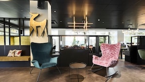 A modern lobby with a reception desk, two chairs, a small table, and a large abstract wall art piece. - Top Hotel Rhoenkitz Bad Kissingen (Bad Kissingen)