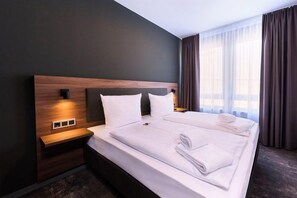 Una habitación de hotel con una cama grande, una mesita de noche y una ventana con cortinas.