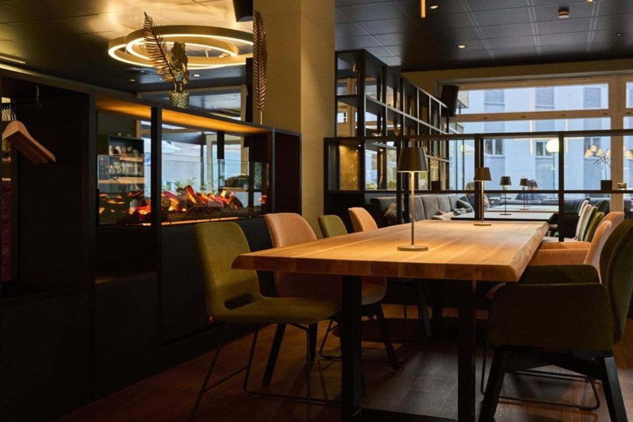 Un espace de restauration moderne avec une longue table en bois, des chaises confortables et une vue dégagée grâce à de grandes fenêtres.