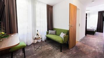 A modern room with a green sofa, a wooden door, a small round table with a bottle, and a bed in the background.