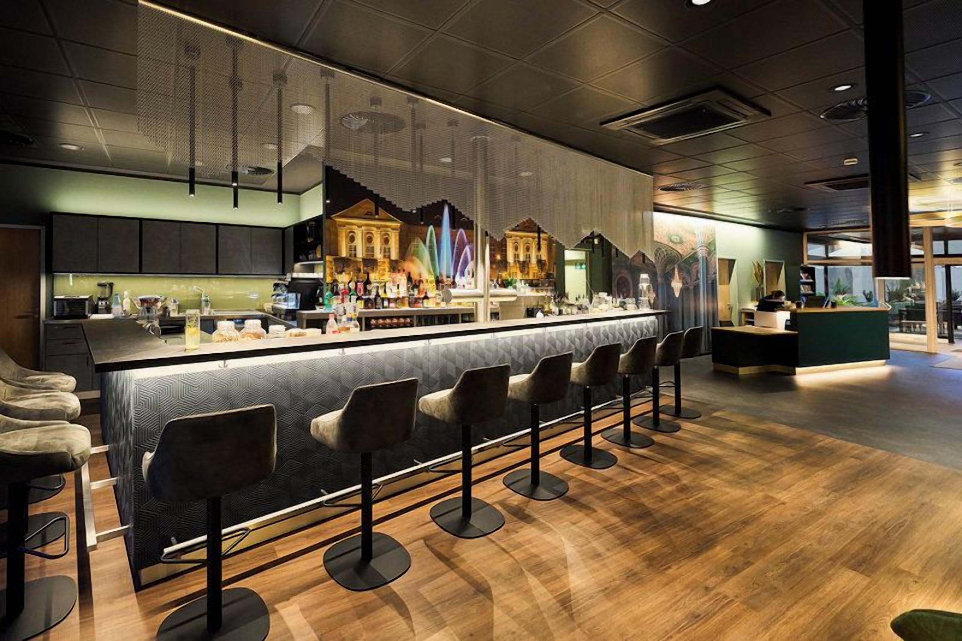 Eine moderne Bar mit einer langen Theke, mehreren Hockstühlen und einer Wandmalerei.