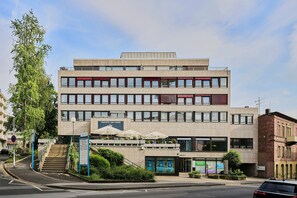 Un edificio de varios pisos con un área de bar o salón en la planta baja, una escalera que conduce a la entrada y un cartel de estacionamiento.