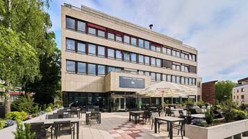 A multi-story hotel with outdoor seating and a garden area.