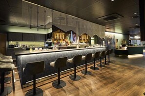 A modern bar area with a long counter, multiple stools, and a decorative wall mural.