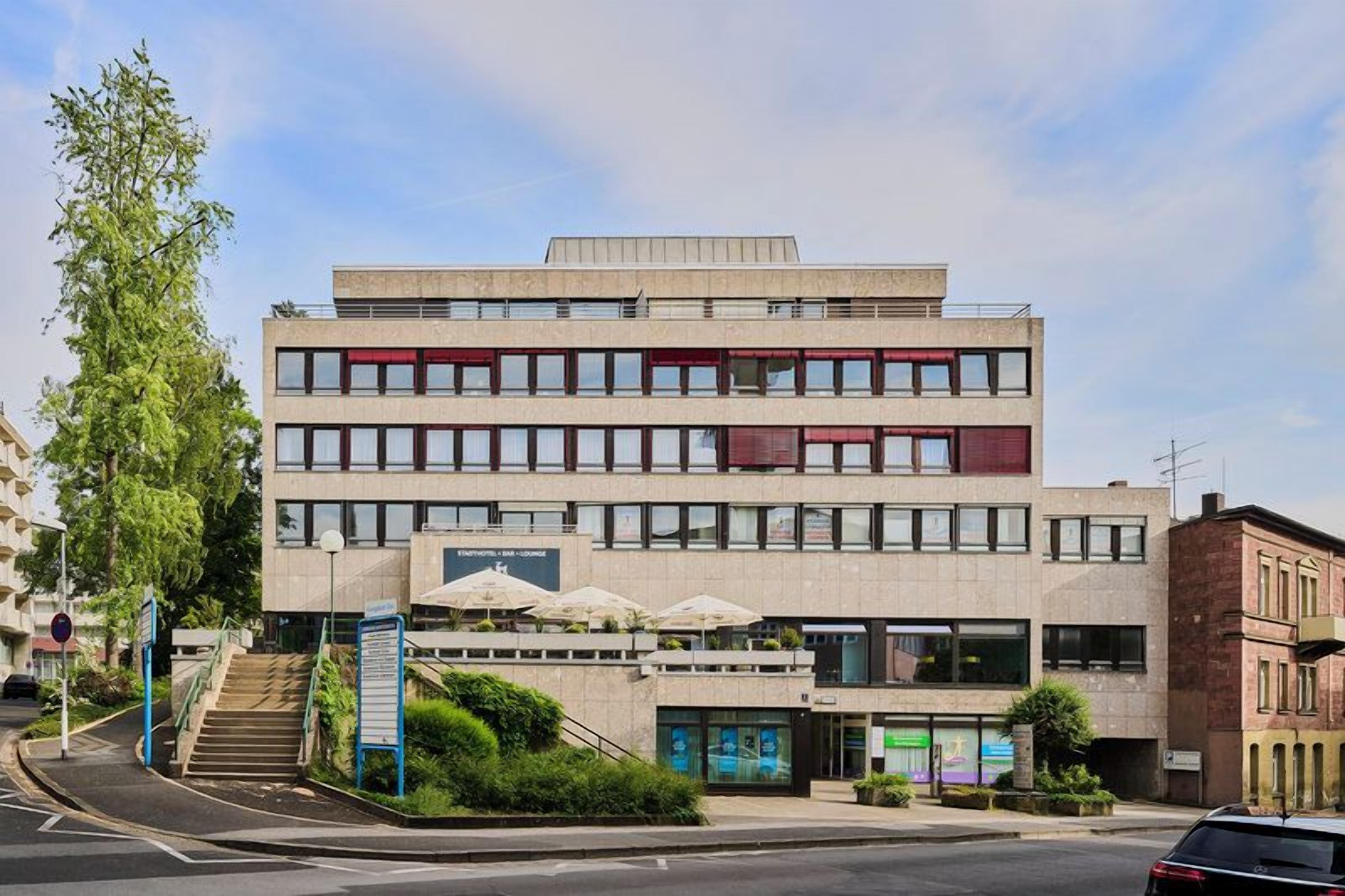 A multi-story building with a flat roof, large windows, and a staircase leading to the entrance.