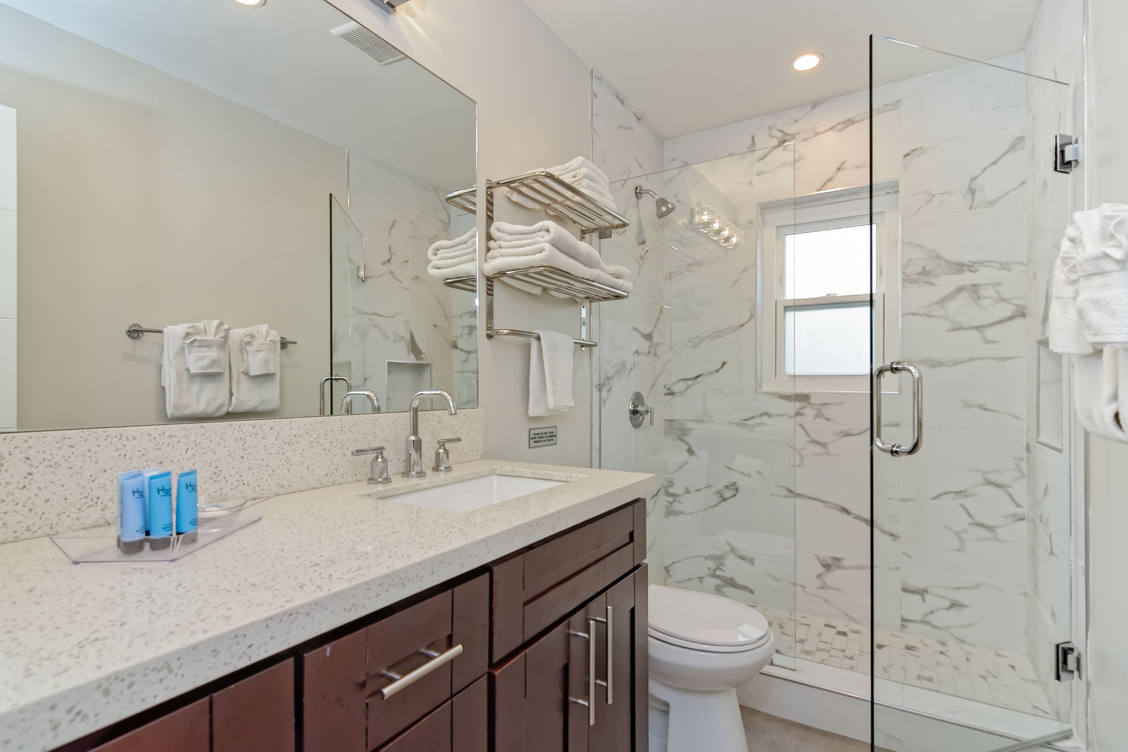 A modern bathroom with a glass-enclosed shower, marble walls, a large mirror, and a vanity with a sink and towel rack.