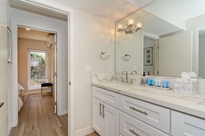Un baño moderno con un espejo grande, muebles blancos y un tocador con artículos de aseo.