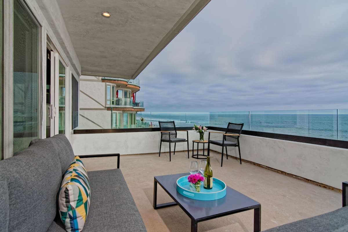 A balcony with a sofa, chairs, a table with a tray, and a view of the ocean.