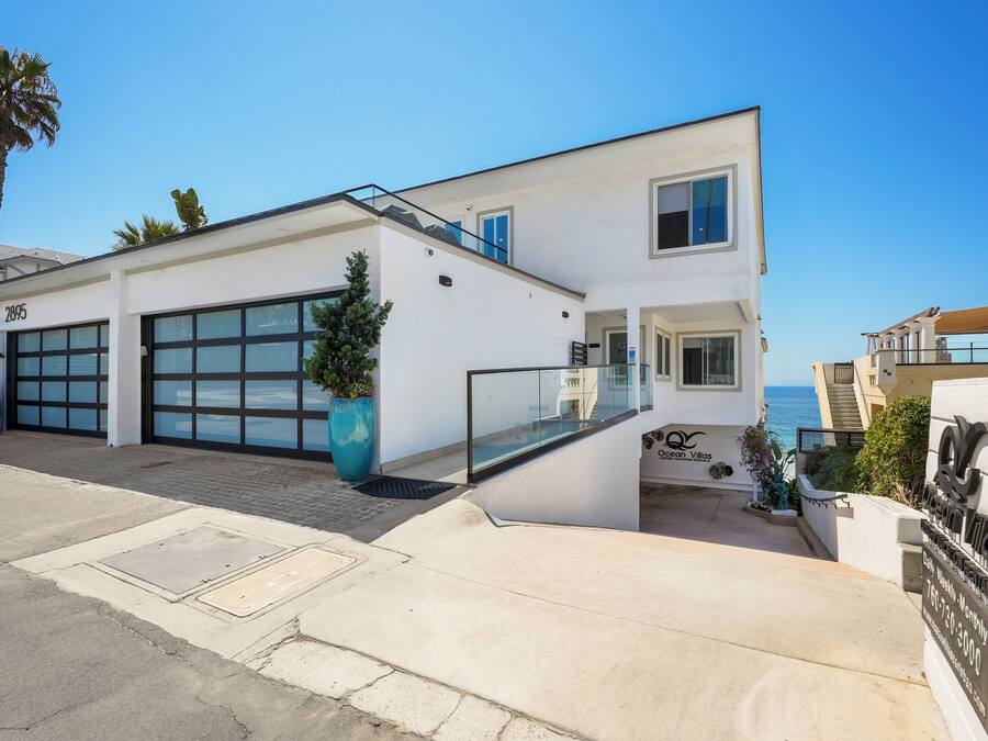 A modern two-story building with a garage, a balcony, and a view of the ocean.