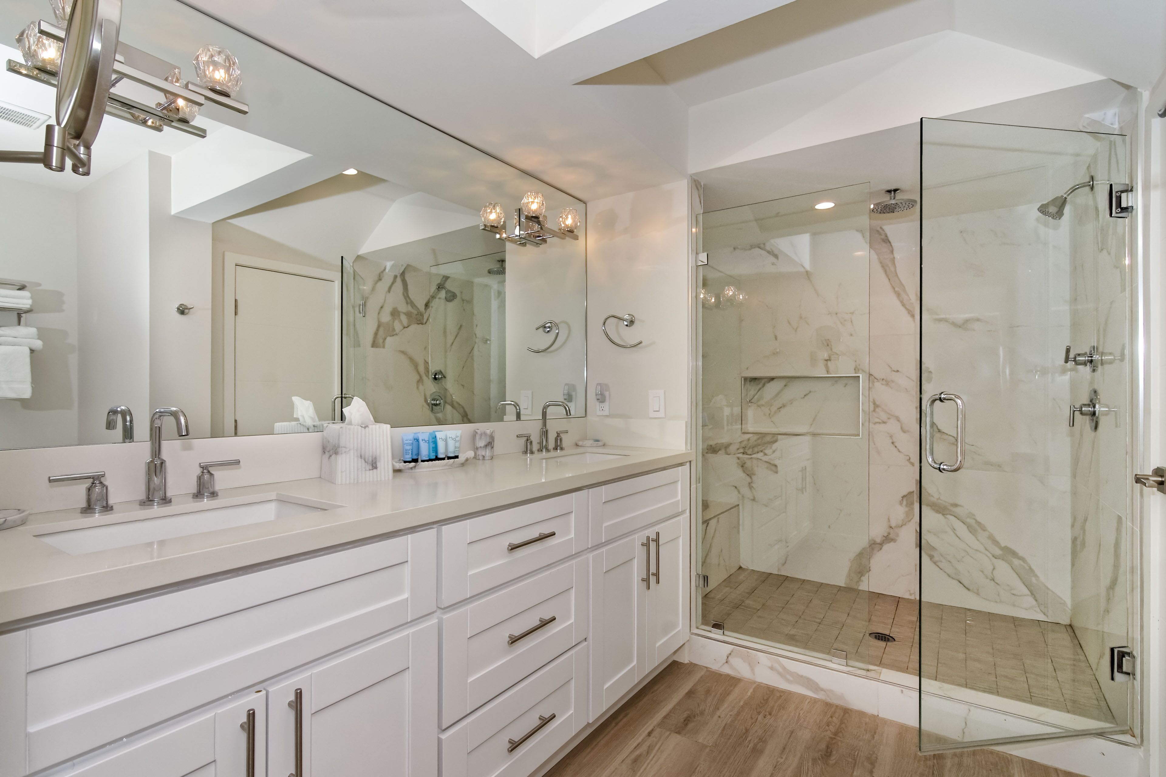 A modern bathroom with a large mirror, a glass-enclosed shower, and a white vanity with multiple drawers.