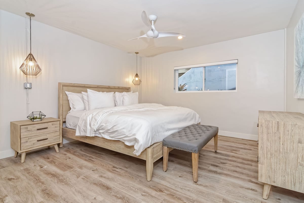 A bedroom with a bed, bedside tables, a bench, a ceiling fan, and a window.