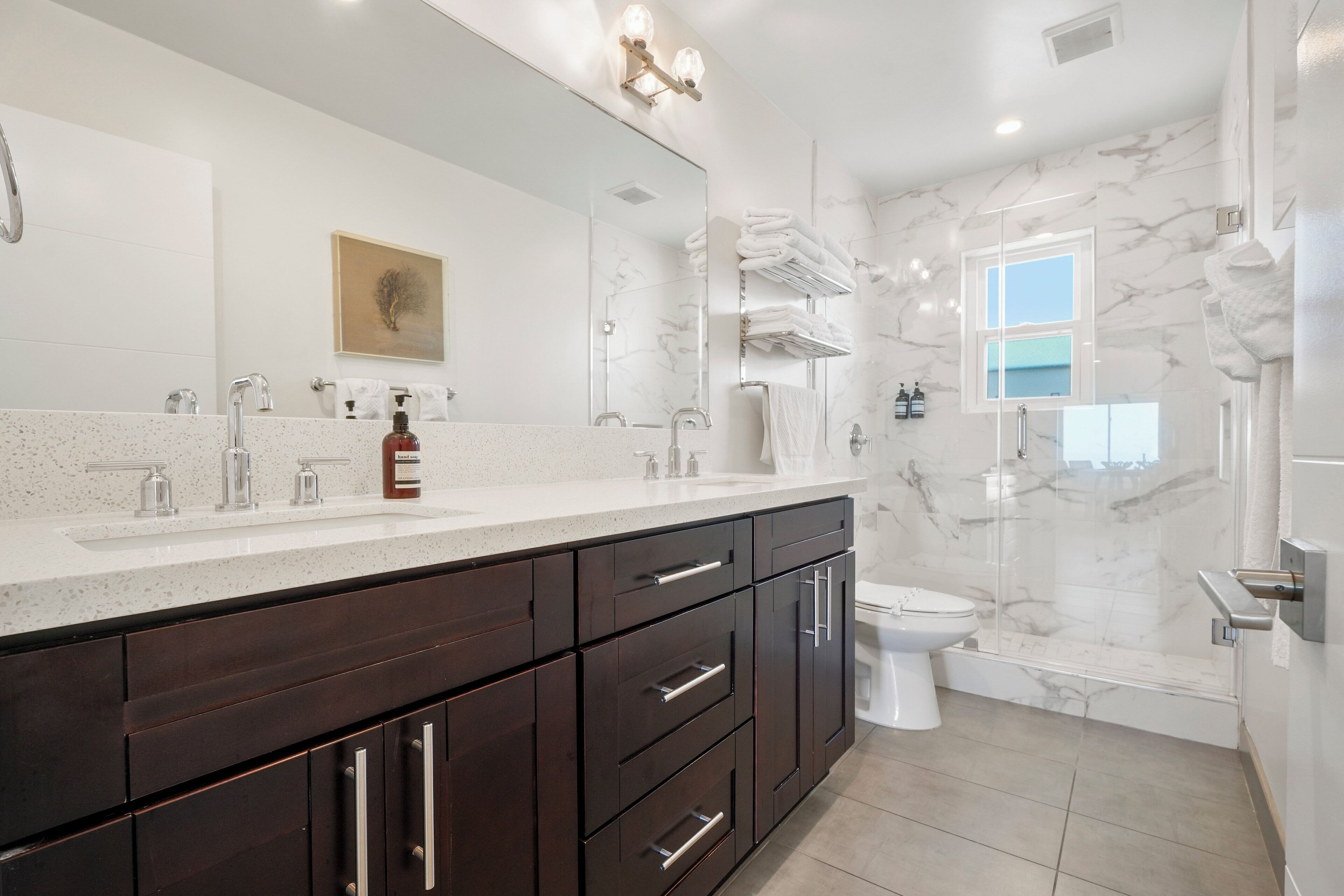 A modern bathroom with a large mirror, dark wooden cabinets, a white sink, and a glass-enclosed shower.