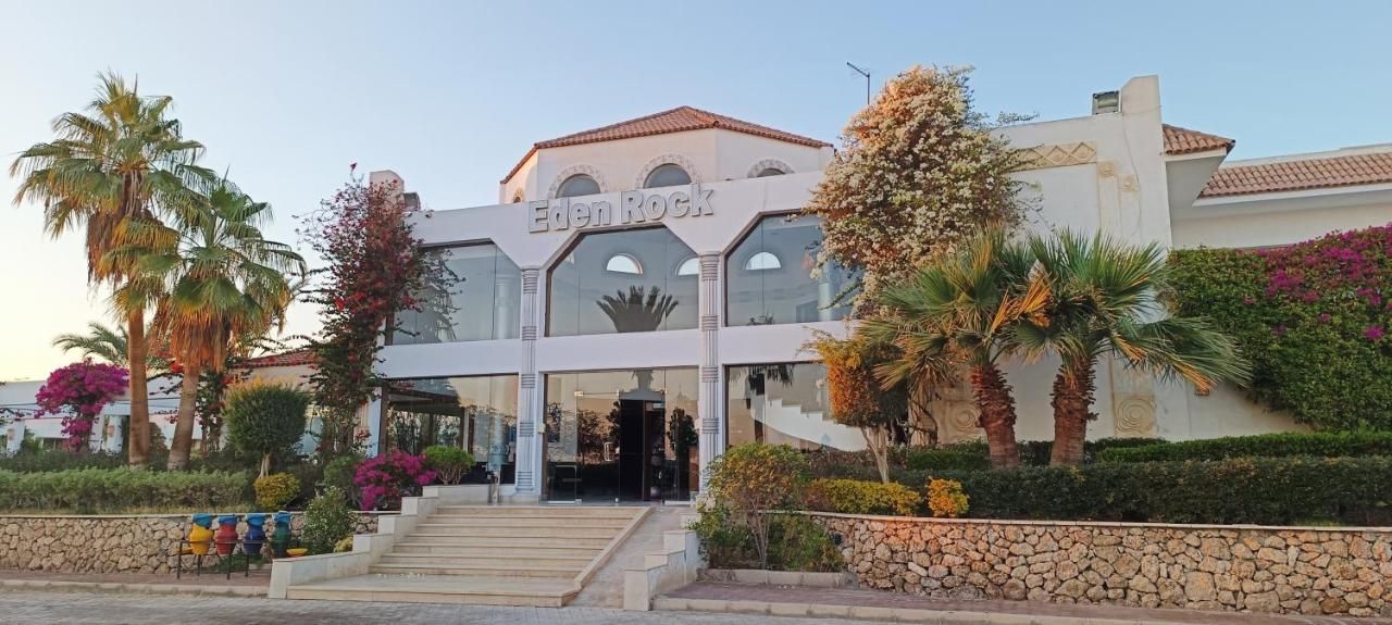 Hotel Eden Rock met een moderne gevel, palmbomen en een stenen muur op de voorgrond.