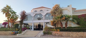 Un hôtel appelé Eden Rock, avec une façade moderne, des palmiers et un mur de pierre en premier plan.