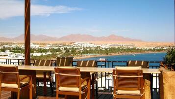 A wooden deck with outdoor seating overlooking a coastal view with mountains in the distance.