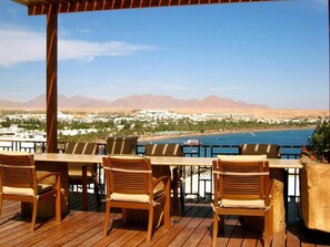 A wooden deck with outdoor seating overlooking a coastal view with mountains in the distance. - Eden Rock Hotel - Sharm El Sheikh (Sharm El Sheikh)