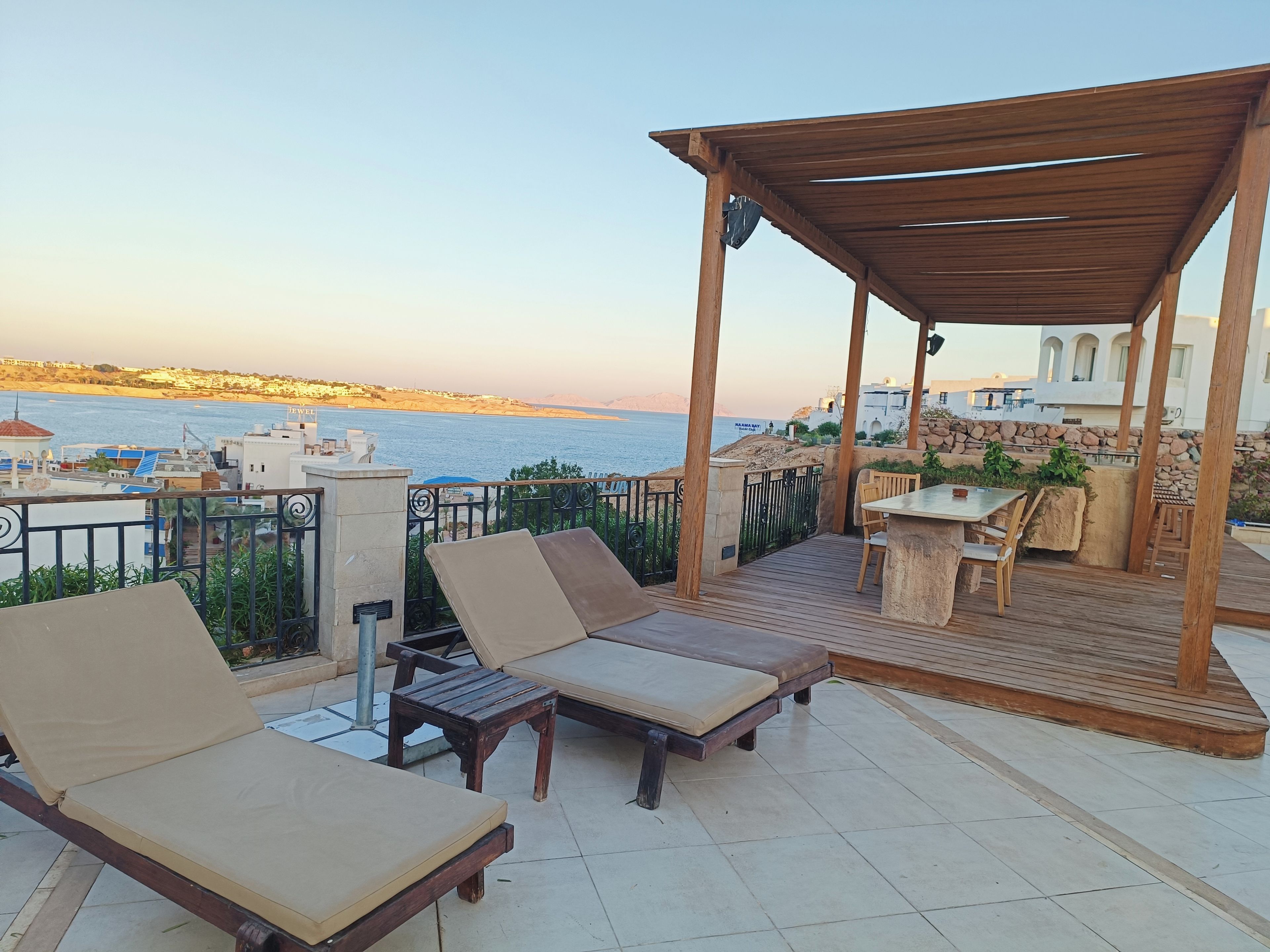 A terrace with wooden furniture, a pergola, and a view of the sea.