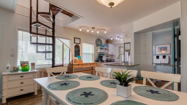 Una cocina amplia con comedor, que cuenta con una escalera en espiral, armarios blancos y una isla central.