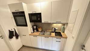 A compact kitchen with white cabinets, a built-in oven, a microwave, and a sink. - FRITZ - Haus Sonnenblick (Diemelsee)