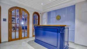 Un área de recepción con mostrador azul, puertas dobles de madera y una pared azul con un emblema decorativo.