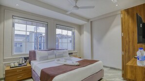 Habitación de hotel con cama, mesita de noche con teléfono y tetera, armario de madera y ventana grande con persianas.