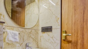 Un baño con pared de mármol, un lavamanos blanco, una puerta de madera y un espejo.