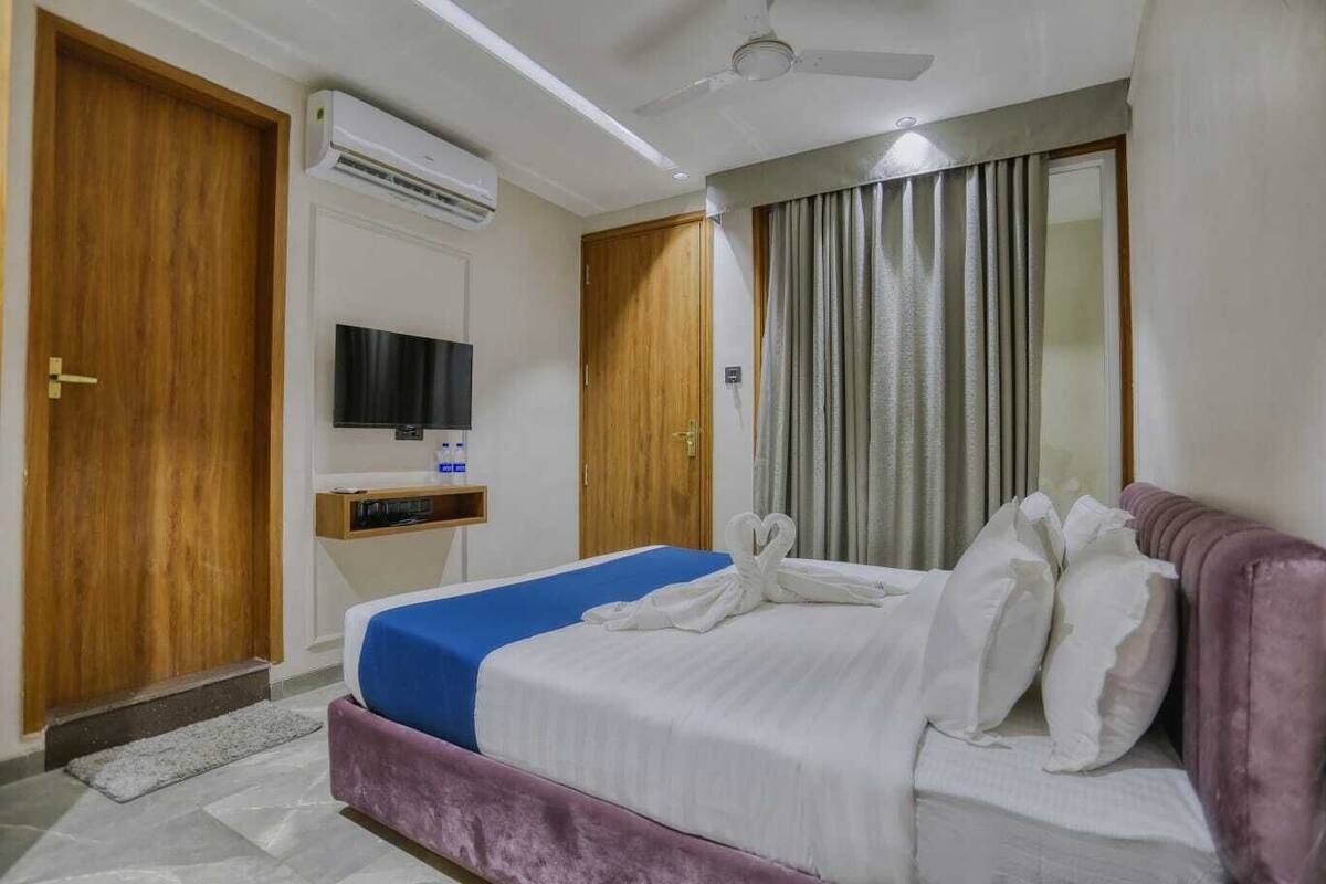Una habitación de hotel con cama, televisión, aire acondicionado y ventilador de techo.