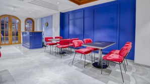 Un comedor moderno con sillas tapizadas en rojo y una mesa negra, un mostrador de recepción de madera y una pared azul decorativa.
