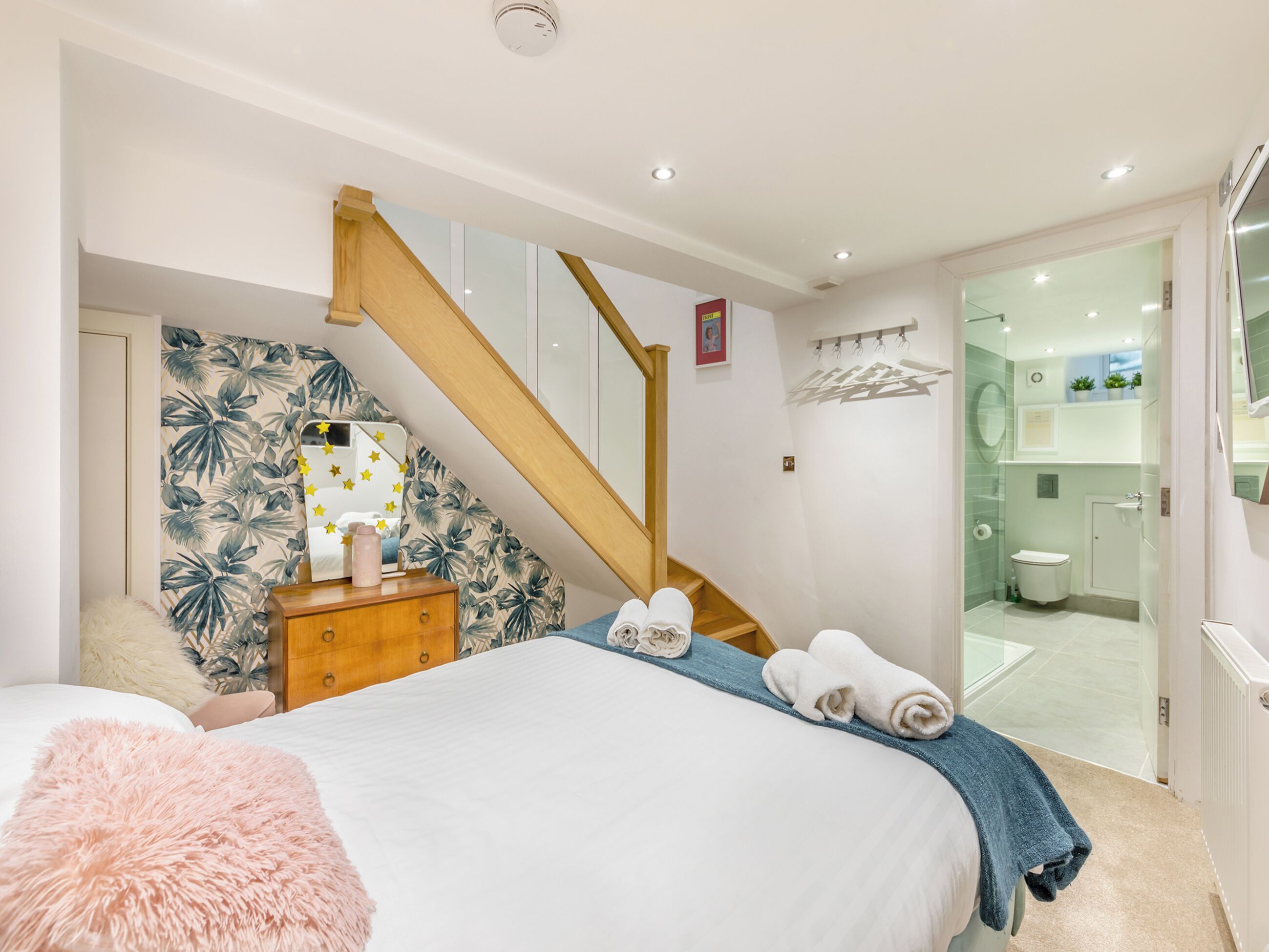 A bedroom with a bed, a wooden dresser, a mirror, and a bathroom visible through an open door.