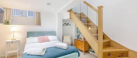 Un dormitorio con cama, mesita de noche, cómoda, escalera y ventana con cortinas.