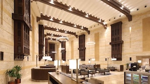 Un hall d’entrée spacieux avec un plafond haut, des poutres en bois et un espace de détente central agrémenté de tables et de chaises.