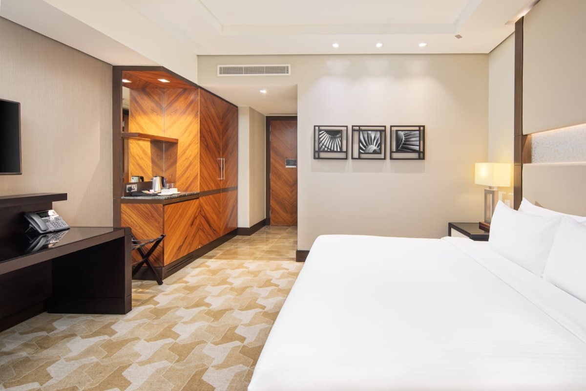 Una habitación de hotel con una cama, un escritorio con teléfono, un minibar y un televisor montado en la pared.