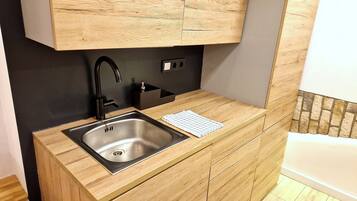 A kitchen with a stainless steel sink, wooden cabinetry, and a black faucet.