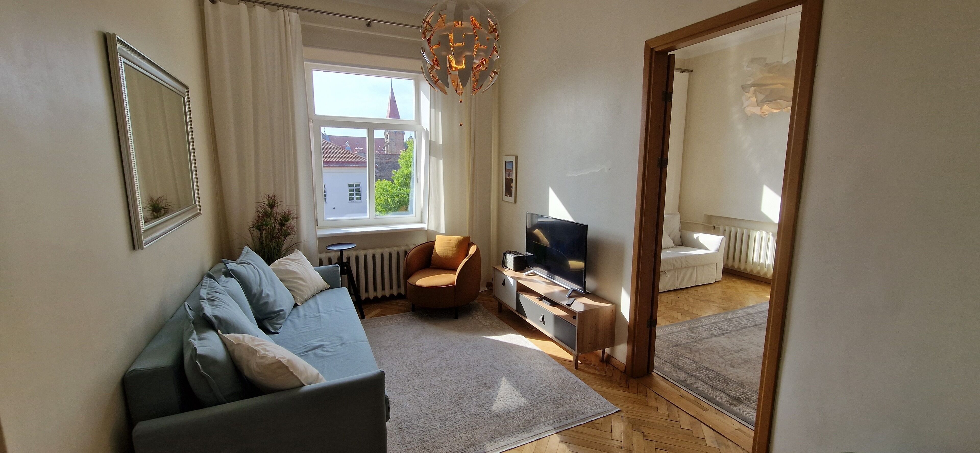A modern living room with a sofa, TV, and a view of a building outside.