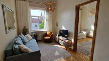A modern living room with a sofa, TV, and a view of a building outside.