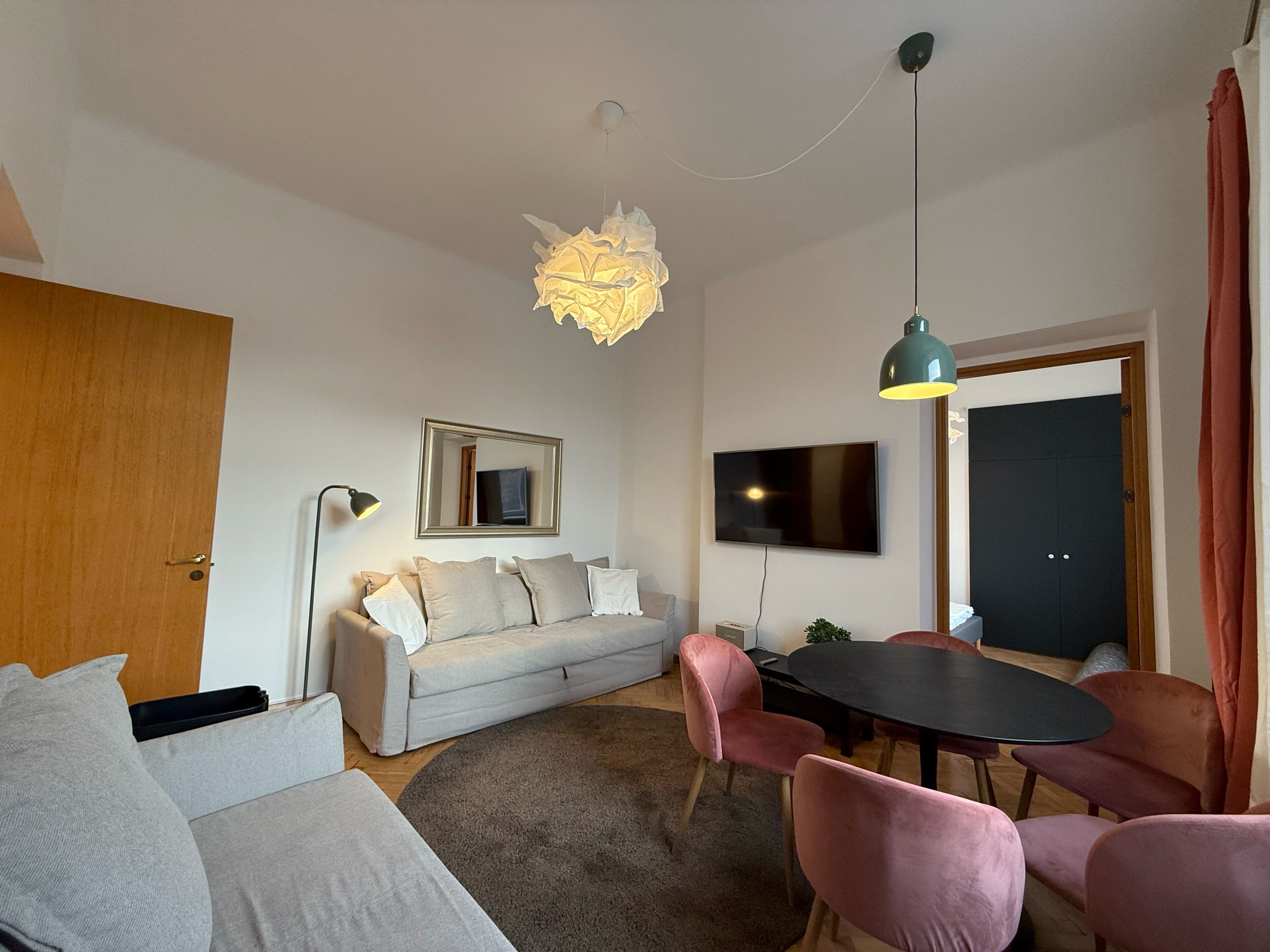 Una sala de estar moderna con un sofá, una mesa de comedor con sillas, un televisor y una lámpara de techo original.
