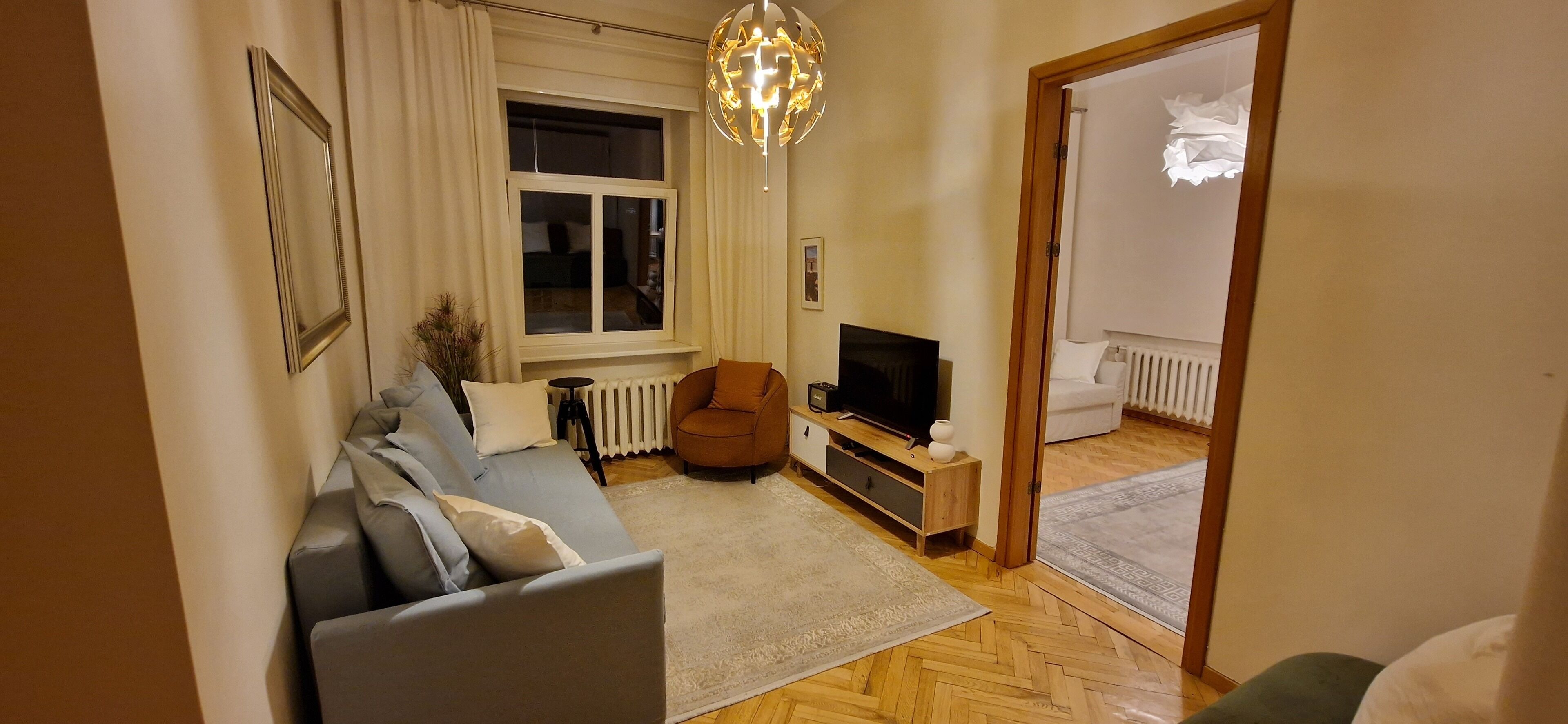 A living room with a sofa, a television, a wooden cabinet, and a radiator.