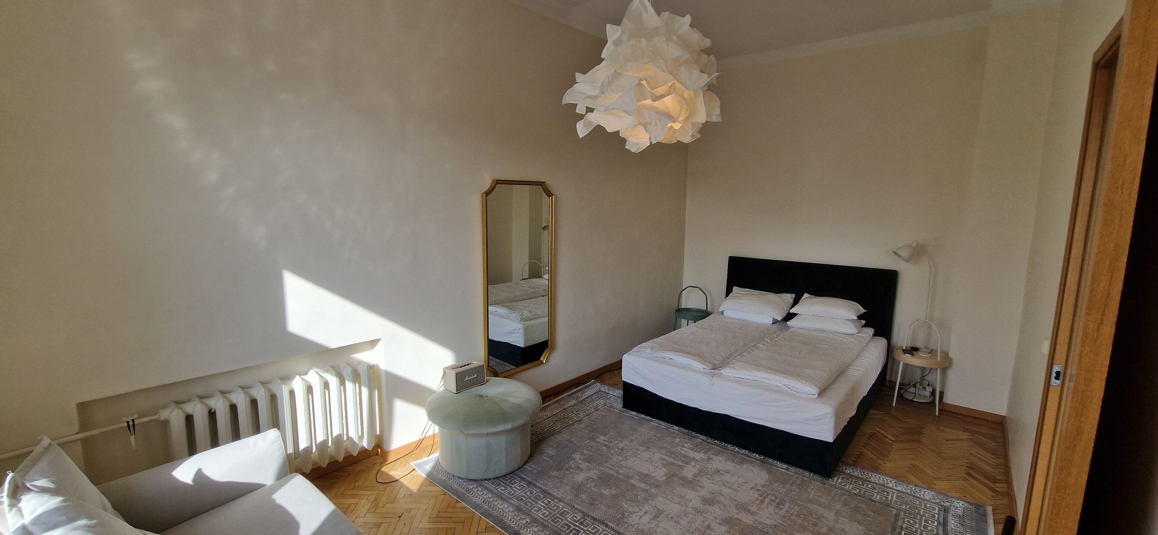 Een slaapkamer met een bed, een radiator, een spiegel, een nachtkastje en een hanglamp.