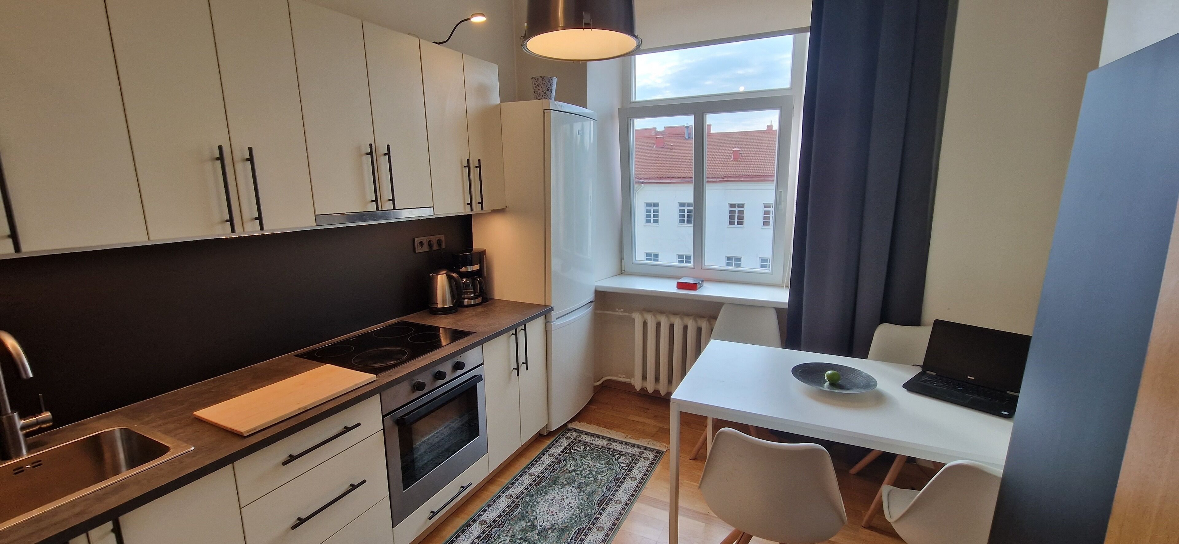A compact kitchen with white cabinets, a stove, and a small dining area with a laptop.