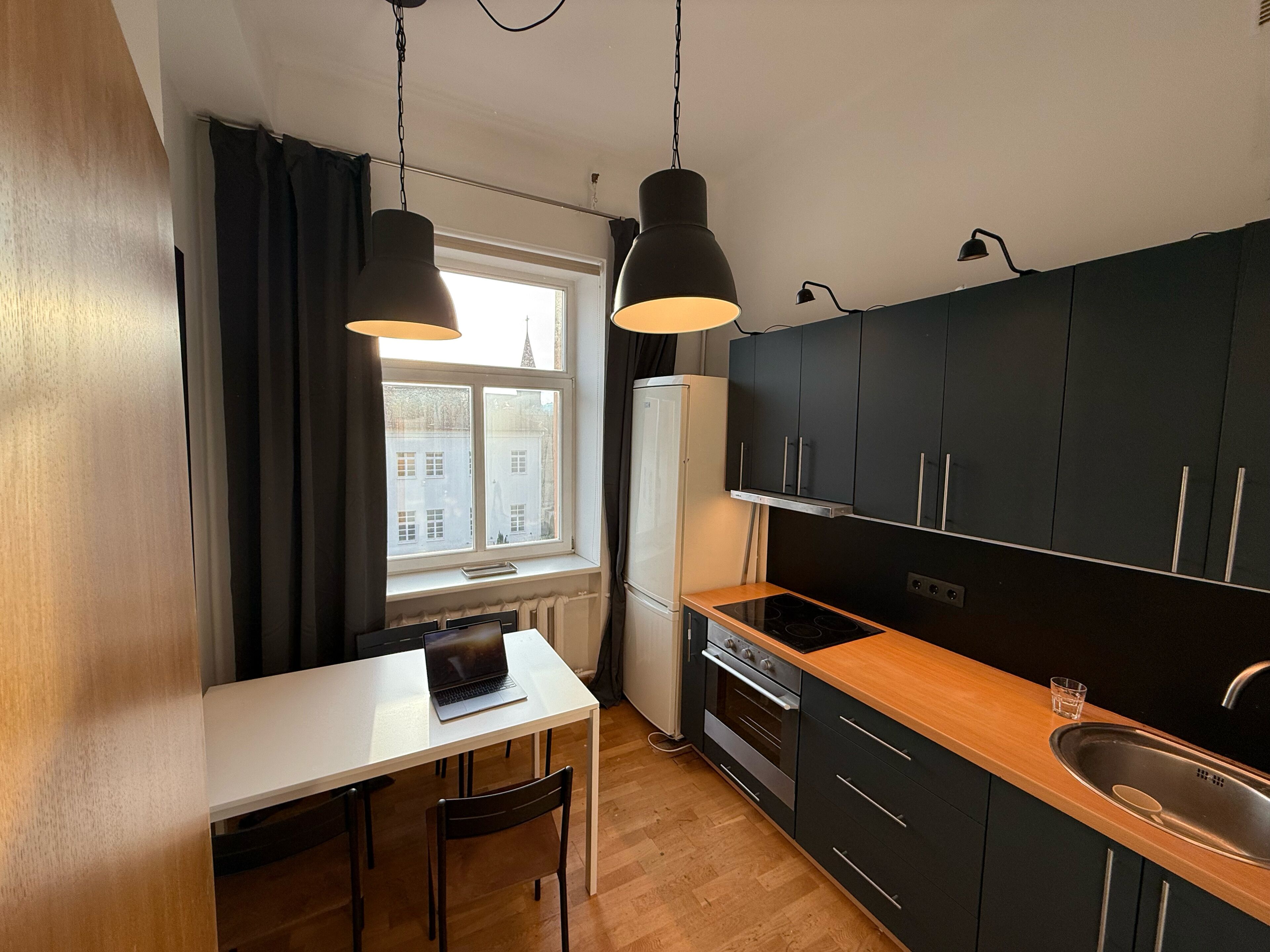 A modern kitchen with a white countertop, black cabinets, and a window with curtains.