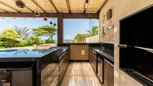 A modern kitchen with a large island, a view of the ocean, and a bamboo ceiling. - Mansão Pé na Areia de Geribá com 6Suítes (Búzios)