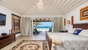 A bedroom with a large bed, a view of the sea, and a balcony with chairs. - Mansão Pé na Areia de Geribá com 6Suítes (Búzios)