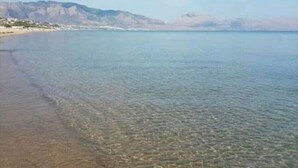 A clear view of a beach with calm waters and distant mountains.