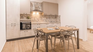 A modern kitchen with a dining area, featuring light-colored cabinetry, a tiled backsplash, and a wooden dining table with chairs. - Charming 2BR in Historic Valletta | Prime Central Location (Valletta)